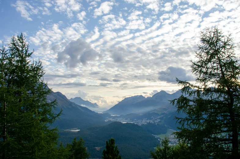 a cloudy sky over some mountains with trees