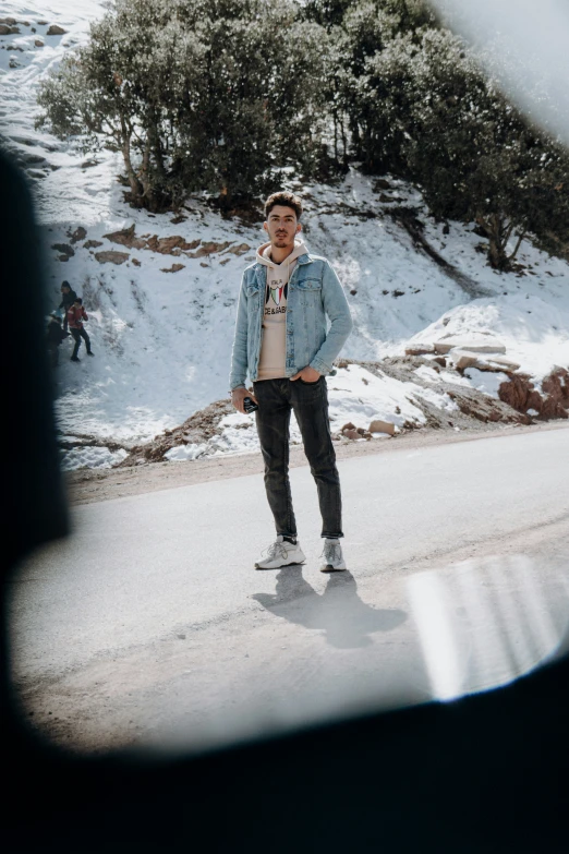 a man in a cap and jeans poses on the side of a road