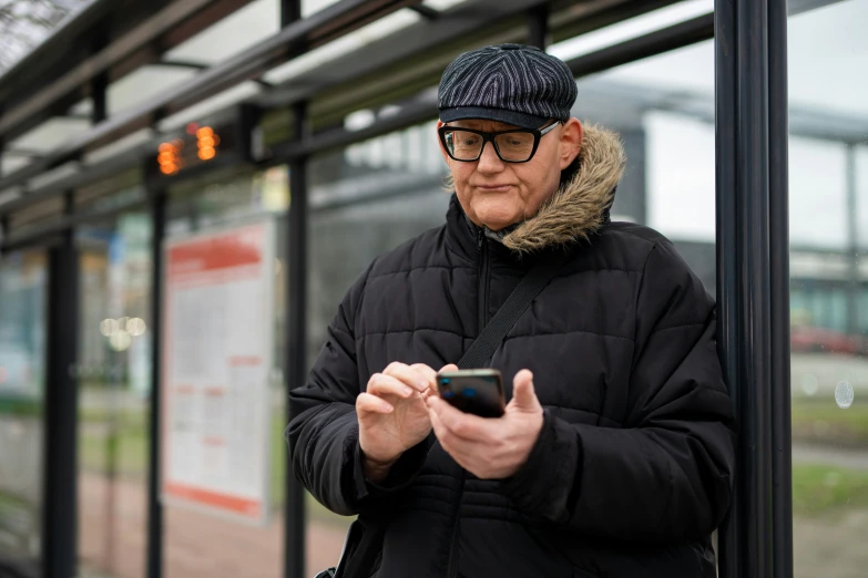 a older man wearing winter clothing while texting on a cell phone