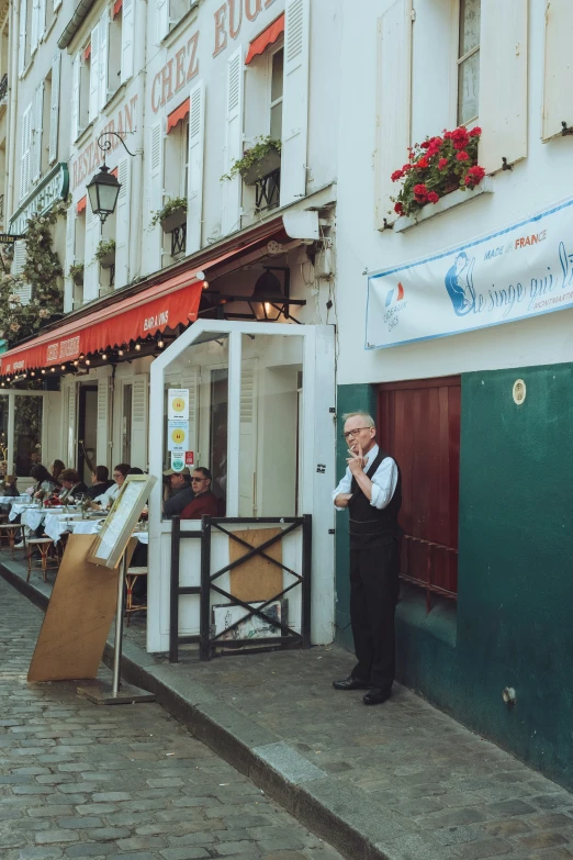 a man stands in front of a restaurant with customers outside