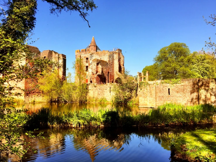 an old castle sitting next to a small lake in front of a forest