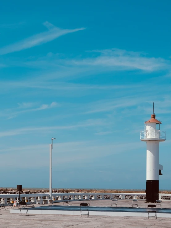 a lighthouse stands on a sandy beach, with benches near by