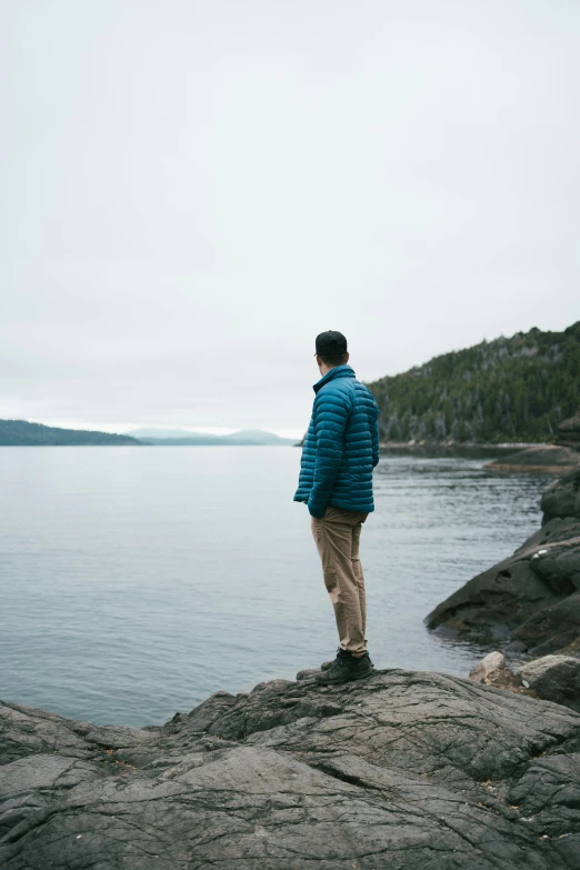 a person wearing a jacket stands on a rock in front of the water