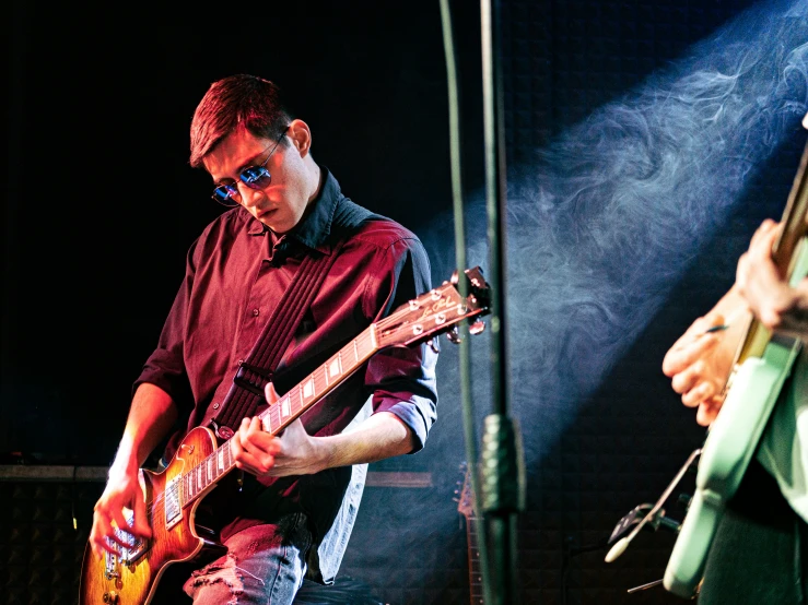 a young man playing a guitar as another plays on a bass behind him