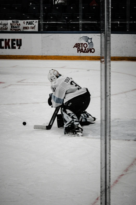 a hockey goalie kneels in the ice as the pucker stops to catch a ball