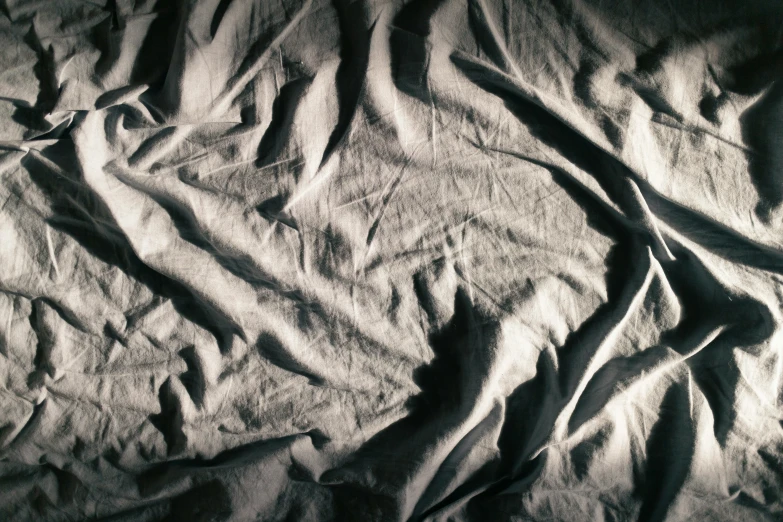 an empty bed in the dark with wrinkled sheet