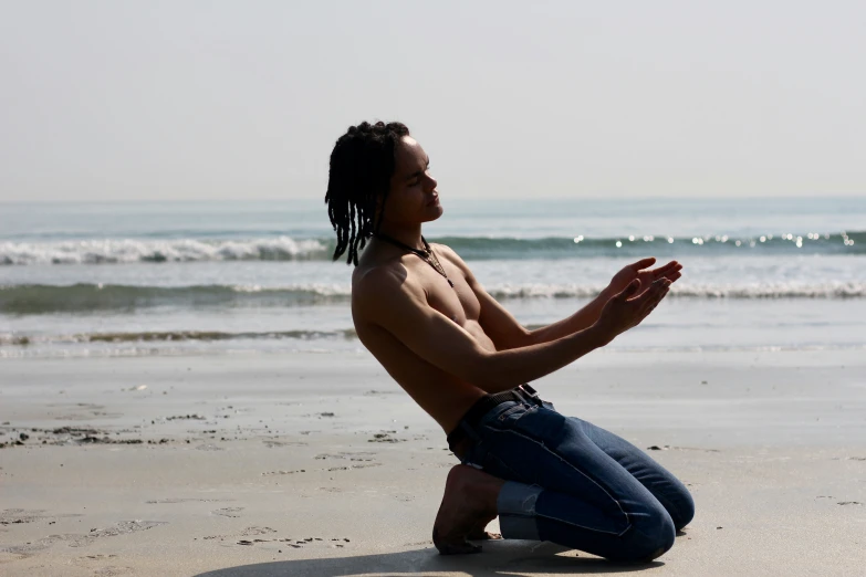 man sitting on beach, meditating with one hand