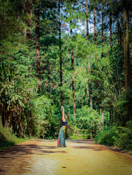 a woman in the middle of a forest holding onto her hat