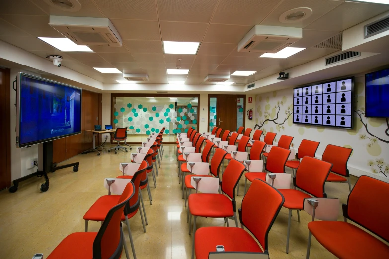 the conference room has many chairs and monitors on the wall