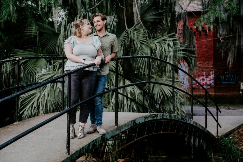 a man and woman are standing on a bridge with palm trees behind them