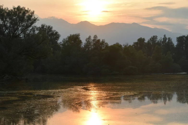 the sun rises over a lake surrounded by wooded area