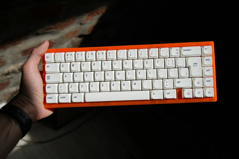 there is a hand holding a keyboard that looks like an orange and white keyboard