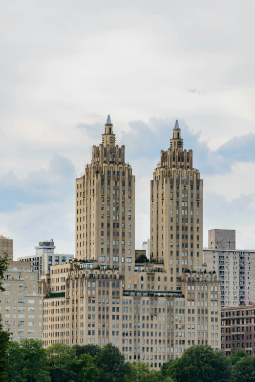 buildings and skyscrs, with trees on the top, are against the backdrop of cloudy sky