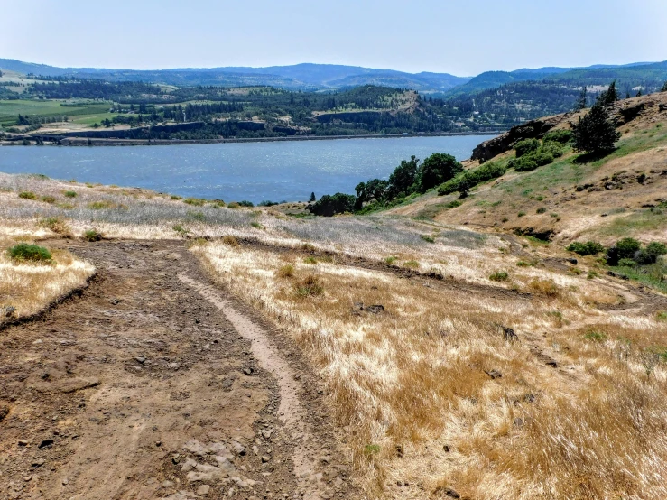 a dirt path near a body of water and mountains
