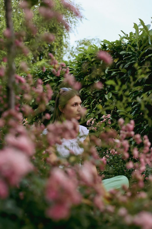 a woman is standing among pink flowers and trees