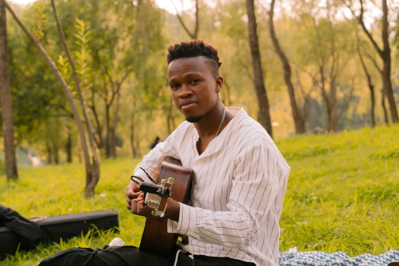 man sitting on the ground holding a guitar and playing an instrument