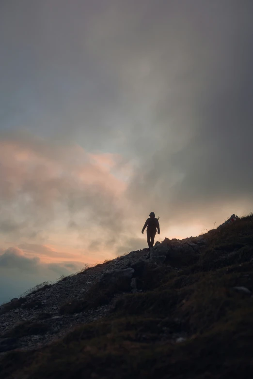 man climbing up the side of a hill under clouds