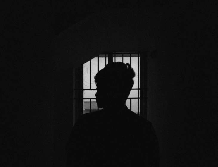 person with curly hair standing near bars of window