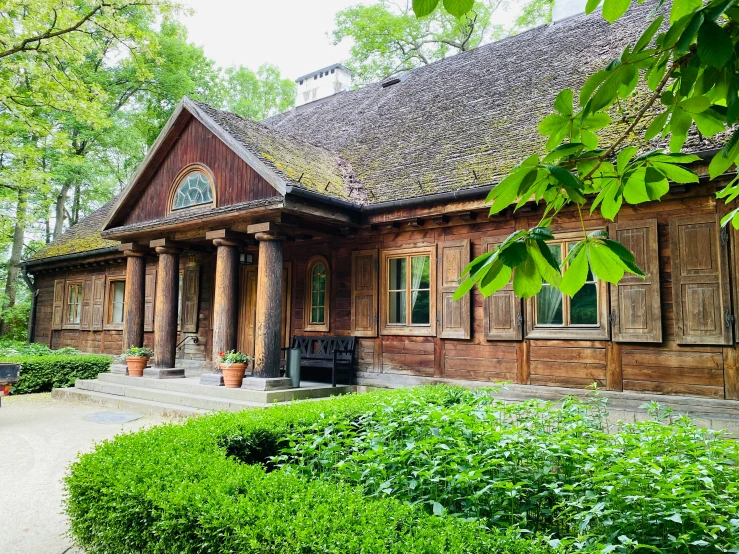 an old wooden building sits in the middle of some green shrubs