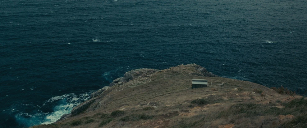 there is a bench in the grass on a hill above the water