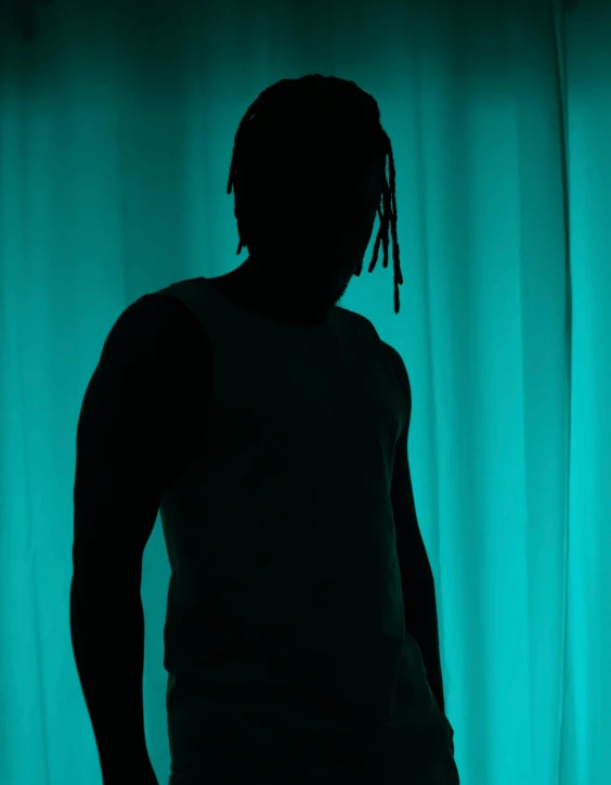 the man is silhouetted against a curtain with green curtains behind