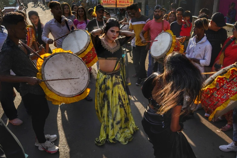 a woman is walking with a group of people playing drum on the street