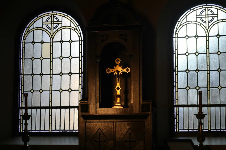 the cross is shining next to three tall stained windows