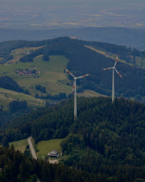 two wind turbines on a hill overlooking some trees