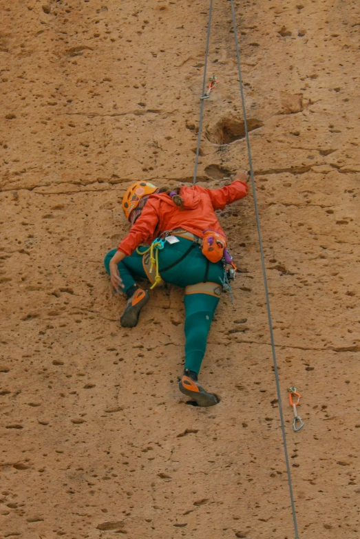 the climber is wearing an orange jacket and climbing rope