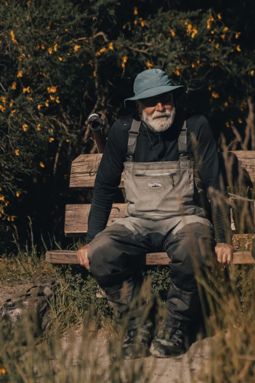 a bearded, old man wearing an apron and hat sitting on a bench