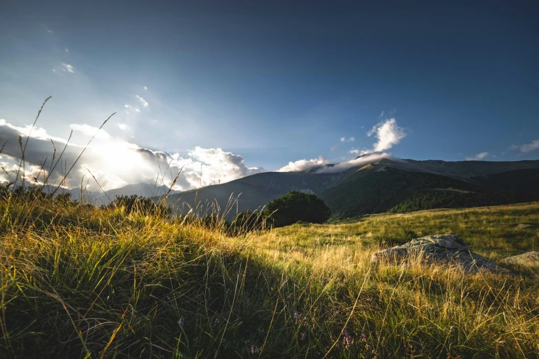 the sun is shining over the grassy hills