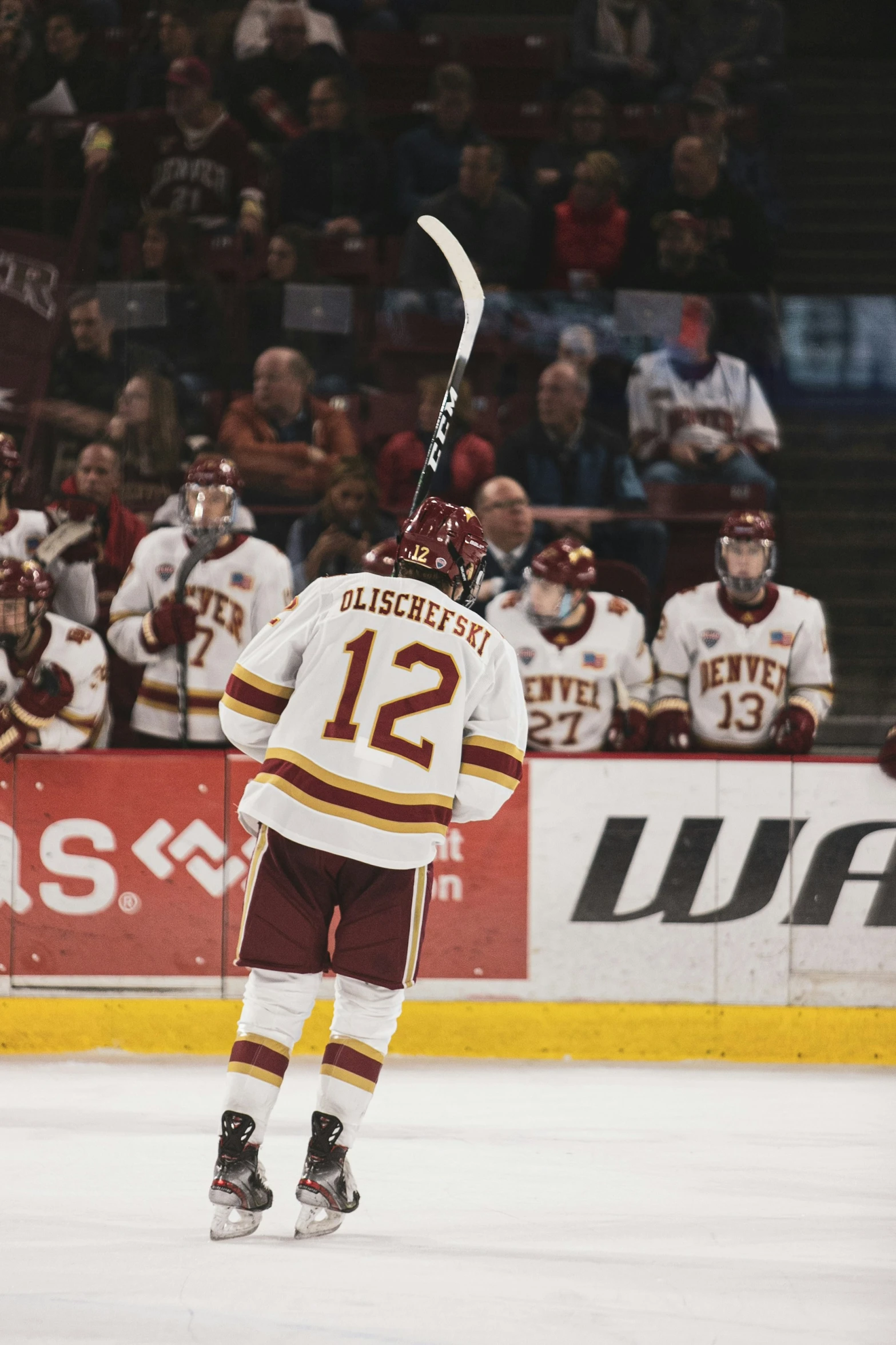 a person in a maroon and white uniform and hockey stick with other people watching