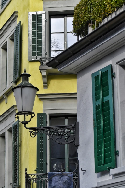 a yellow building has green shutters and a street lamp in front of it