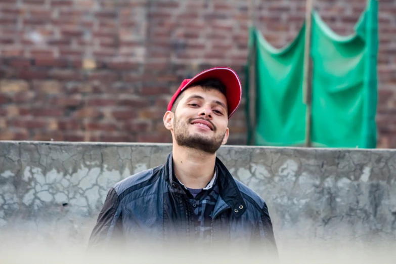 a man in black jacket and red hat by brick wall