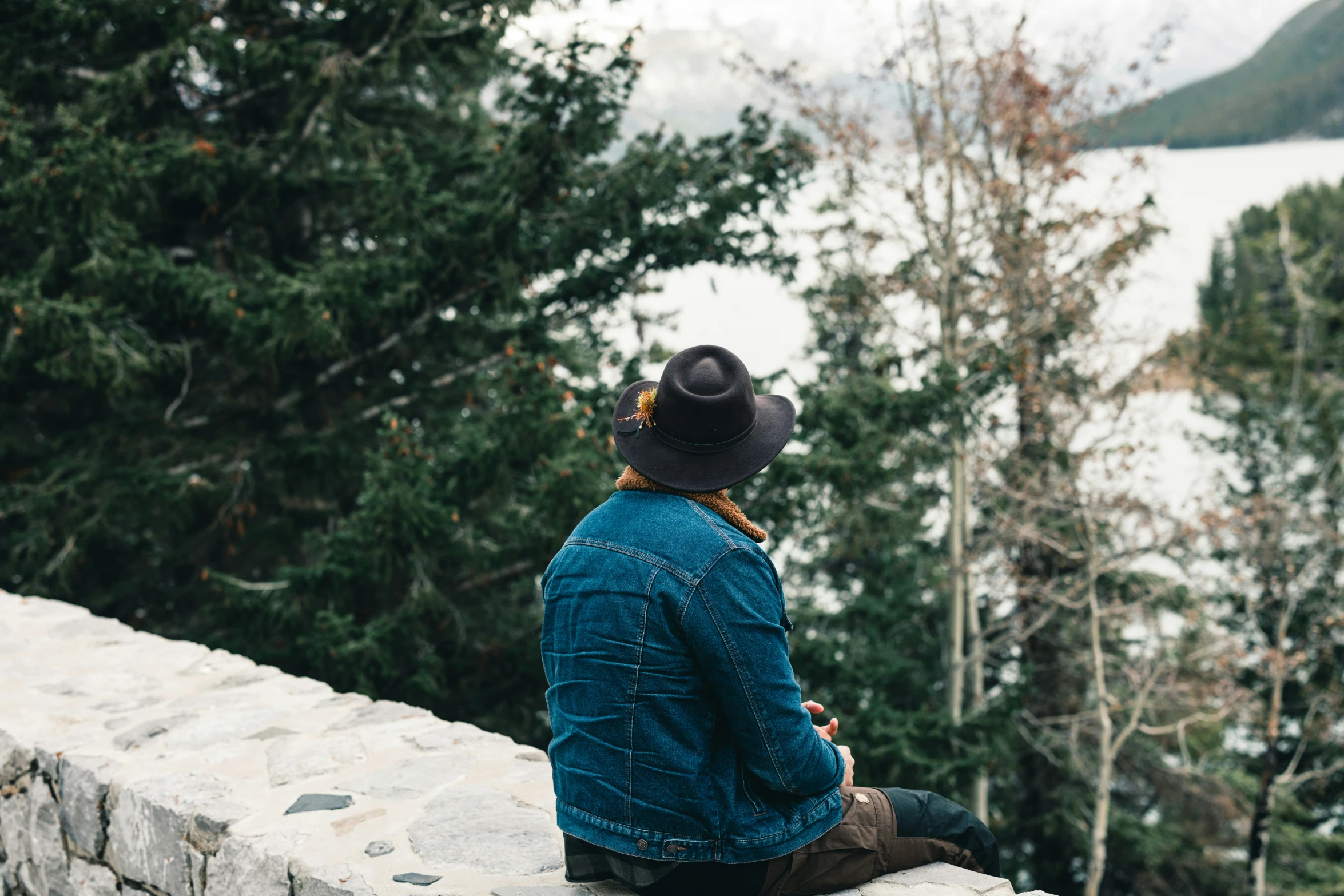 a person with a hat on sitting at the edge of a wall looking at the water