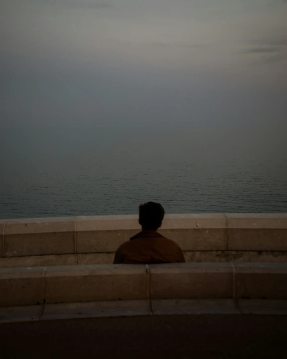 man sitting on concrete bench looking out at the ocean