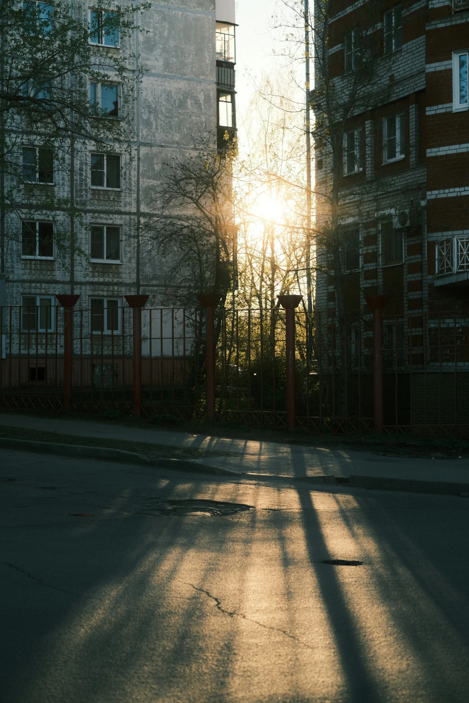 the sun shining through buildings near a fence