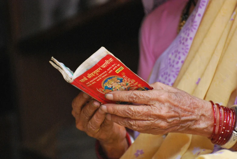 an elderly woman reading a book and putting together celets