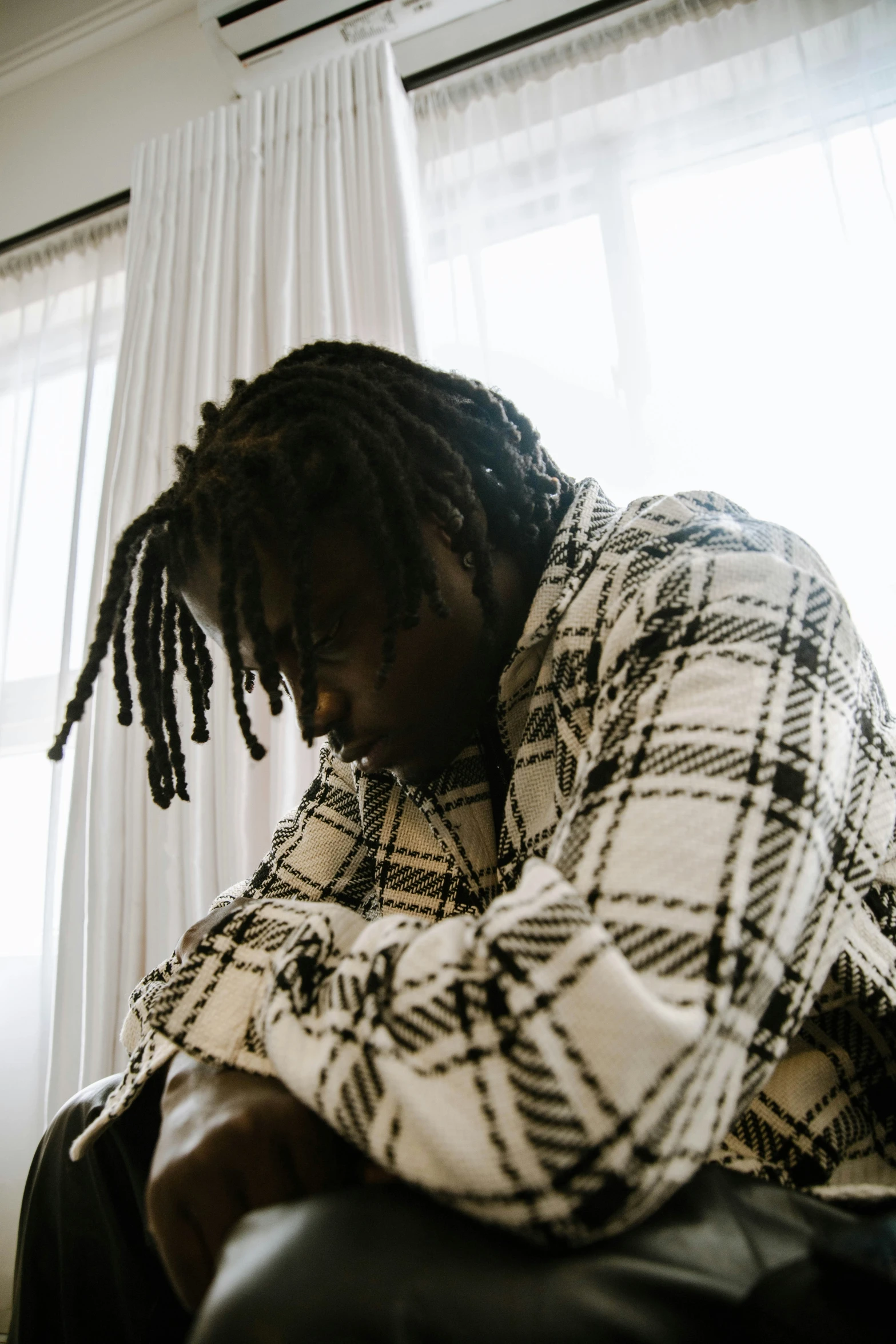 a man sitting in front of a window covered in plaid