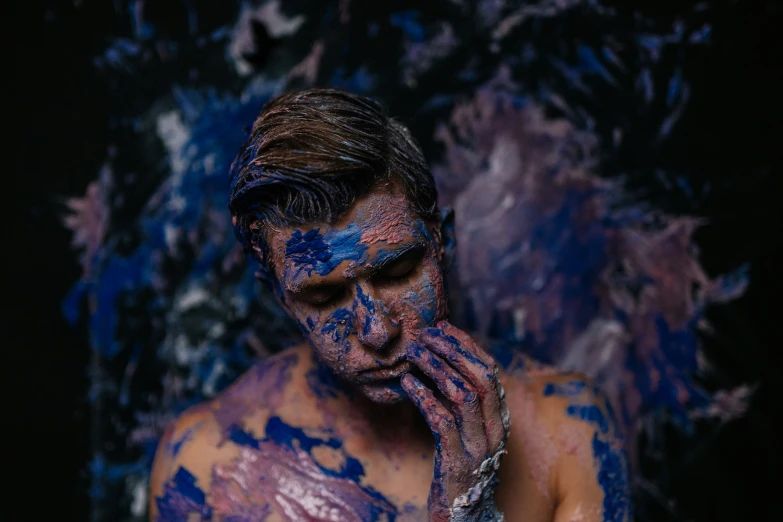a man painted with blue and purple colors and covered with dirt
