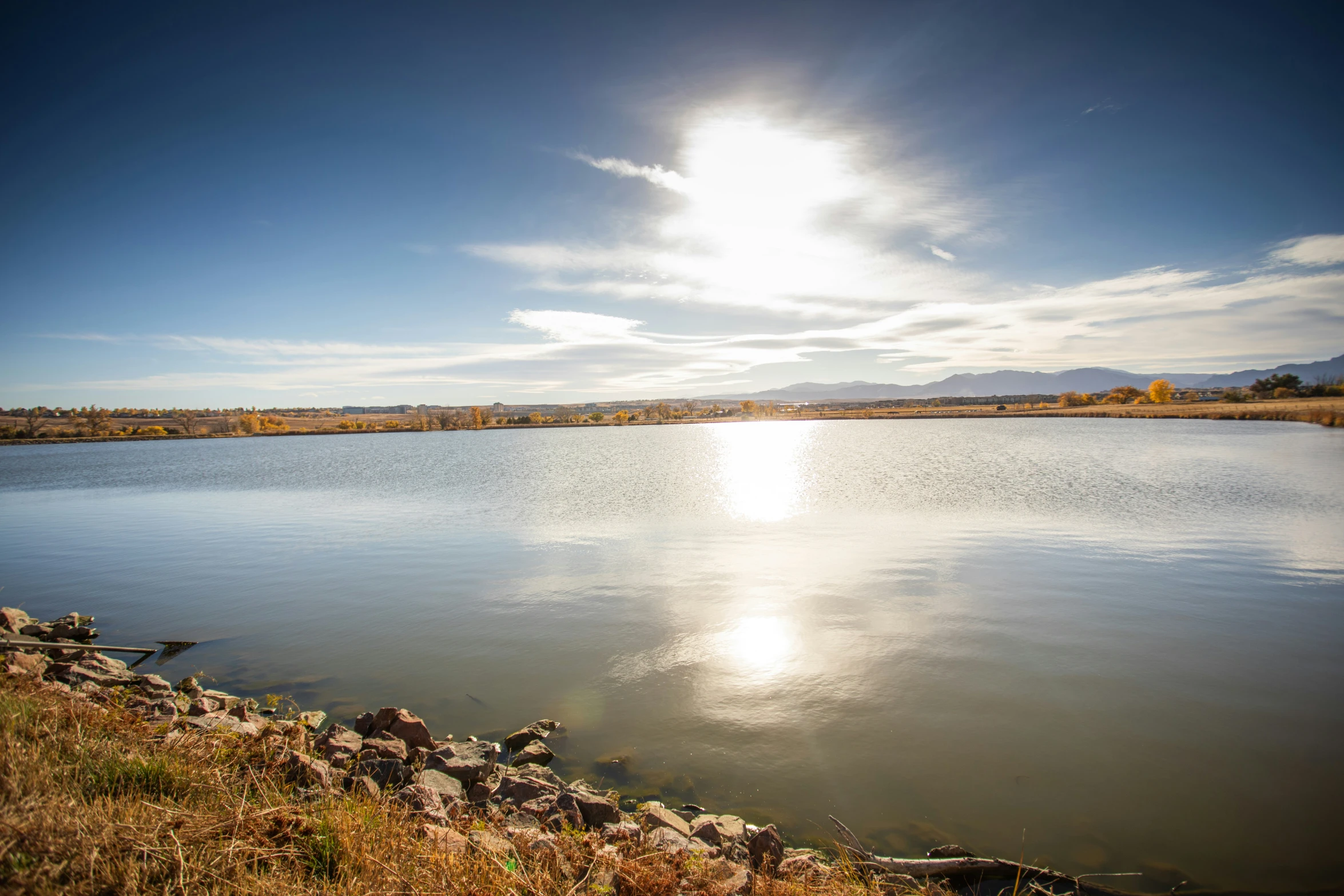 a view of water from the bank with rocks and grass around it