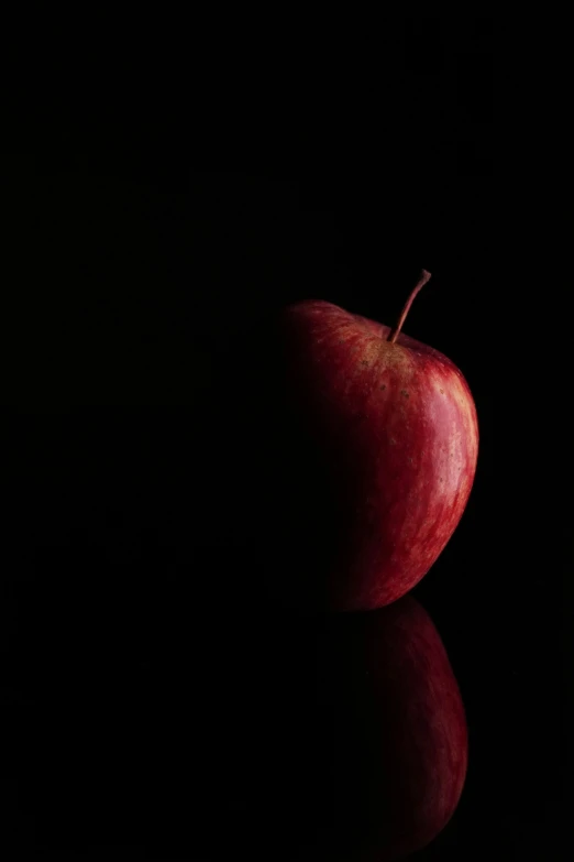 an apple is sitting on a black table with its reflection