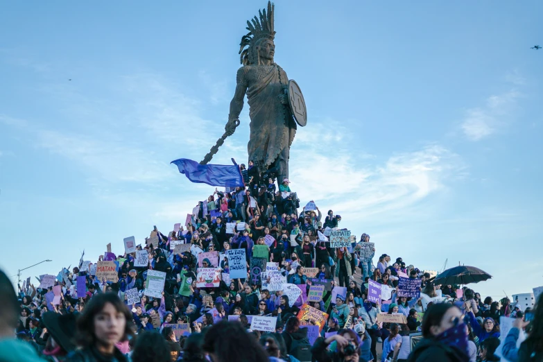 a crowd of people holding signs in front of a large statue