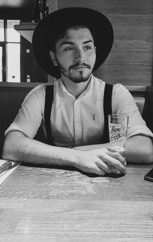 a man wearing a hat sitting at a table with a drink