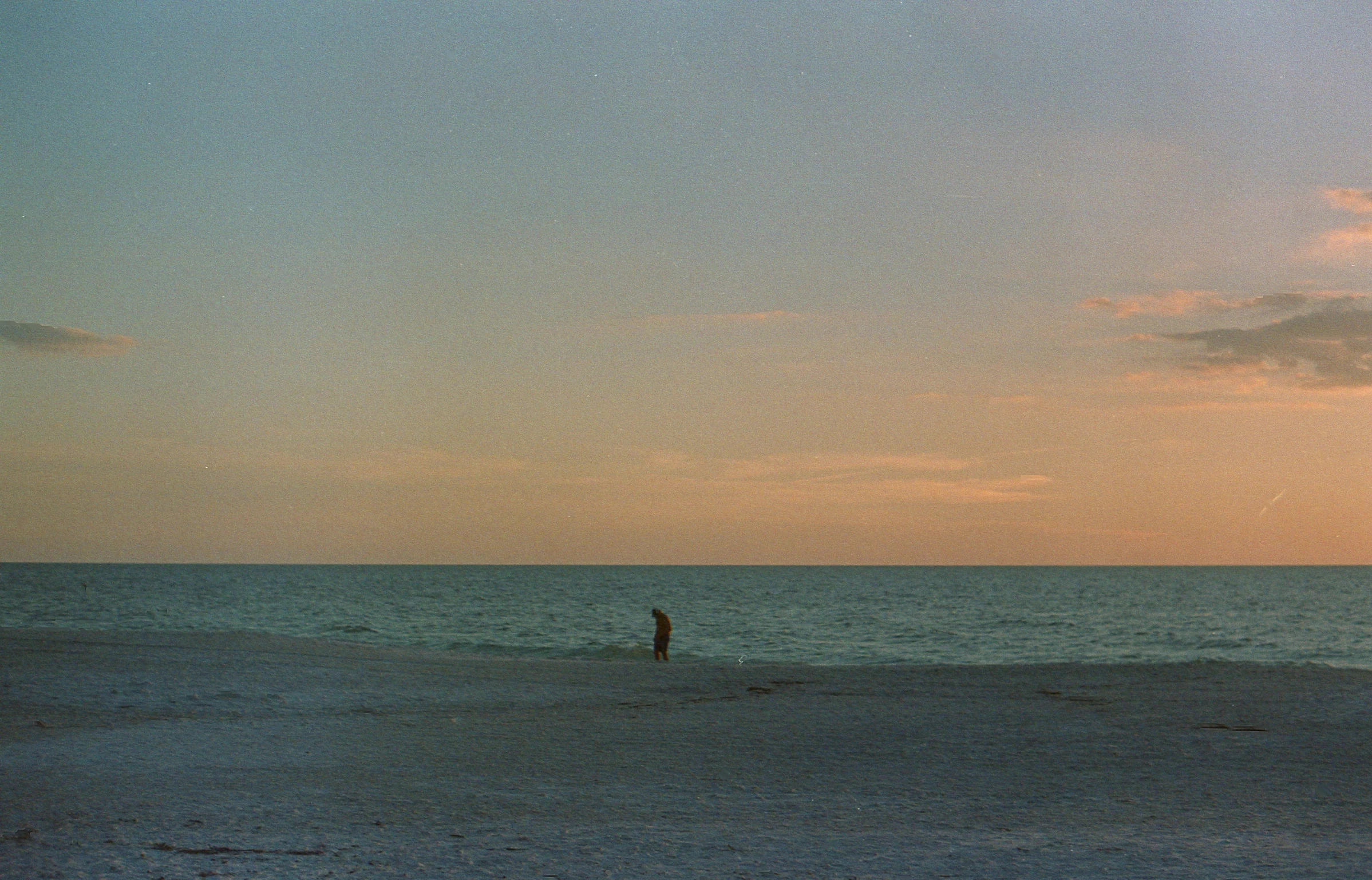 two people are standing in the distance while another person watches from the shore