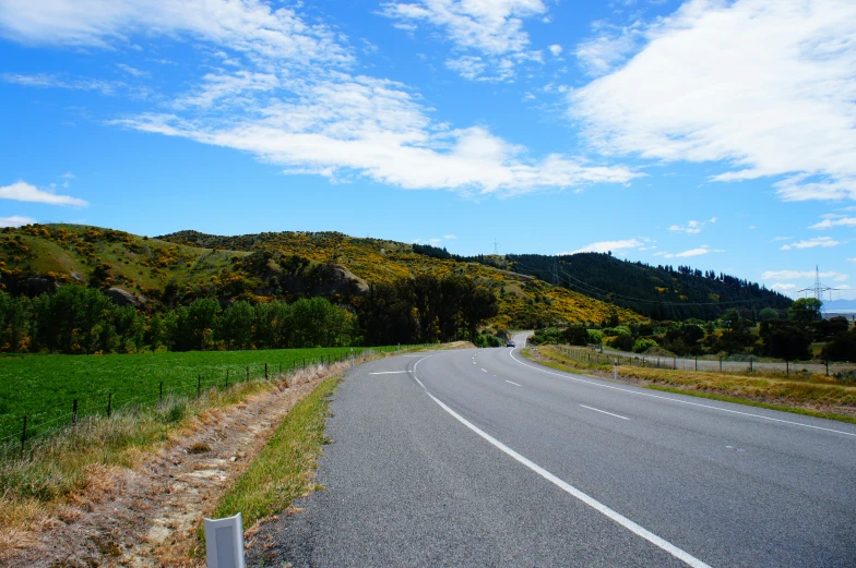 an empty road with trees on the sides and blue sky on the top of the hill