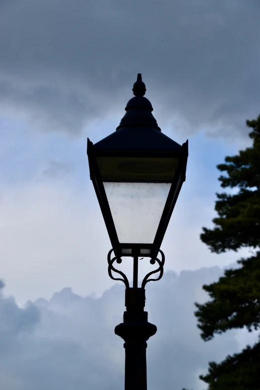 the top of a street lamp in front of a cloudy sky