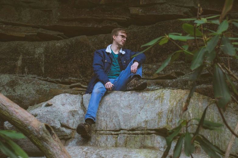 a man sitting on a rock next to some green plants