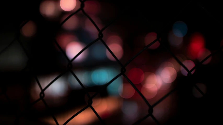 blurred boke - lights as seen through a fence in a park at night