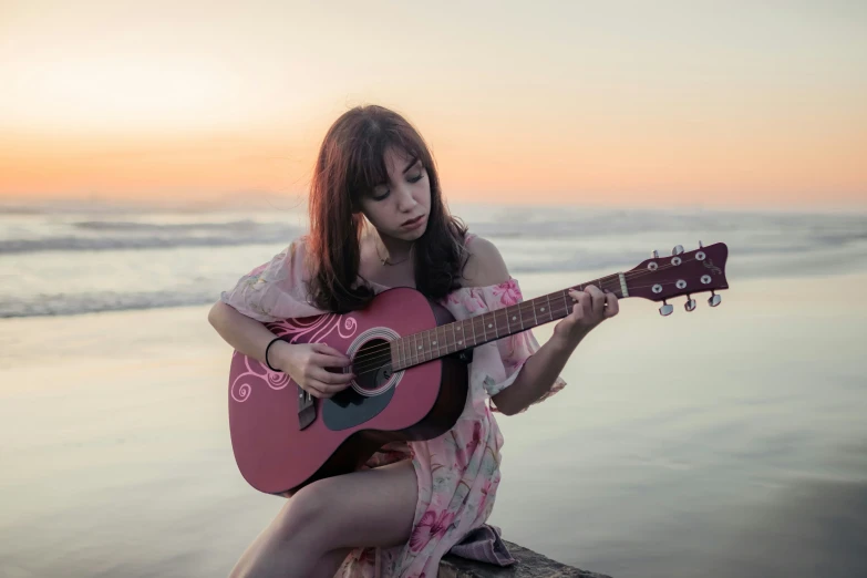 a girl playing guitar on the beach with sunset